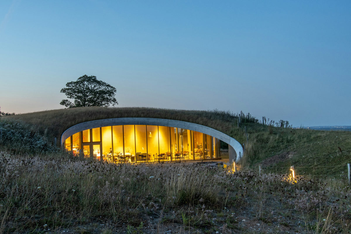 A round building with a grass roof glowing at dusk, set into a hillside