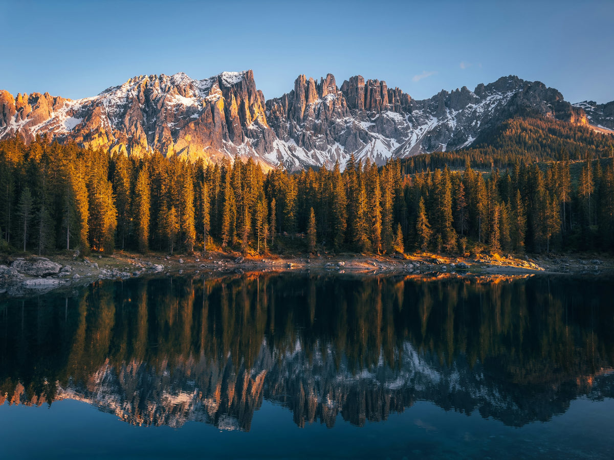 A still alpine lake at dawn perfectly mirroring golden mountain peaks